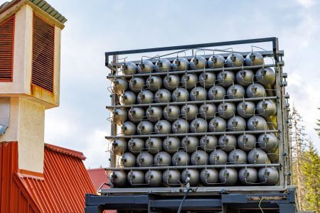 A lot of different small metal bottles filled with gas or gasoline are stacked in large piles and illuminated by the bright warm daytime sun